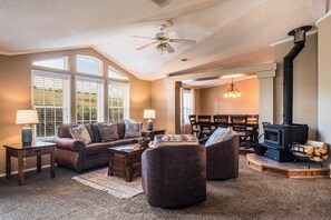 A cozy living room with a fireplace, a ceiling fan, and a dining area with a chandelier. - Angel Fire Home: Sangre de Cristo Mountains View! (Angel Fire)
