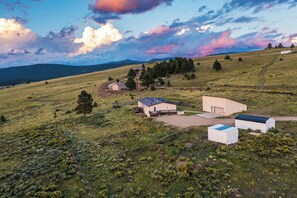 A rural landscape with a small cluster of buildings, including a house and a barn, surrounded by open fields and scattered trees. - Angel Fire Home: Sangre de Cristo Mountains View! (Angel Fire)