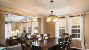 A dining area with a wooden table and chairs, a chandelier, and a view of the outdoors through large windows. - Angel Fire Home: Sangre de Cristo Mountains View! (Angel Fire)