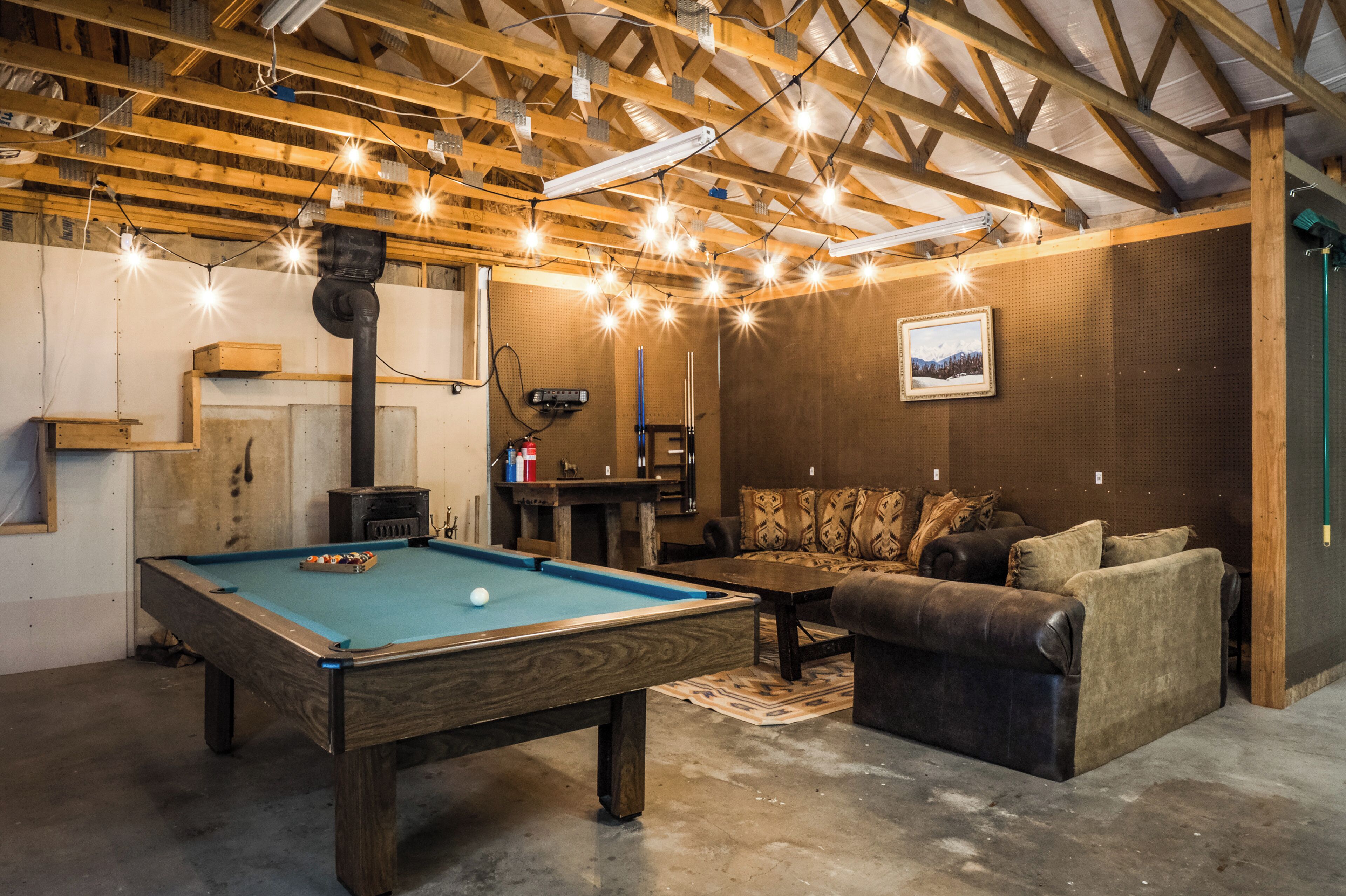 Une table de billard dans une pièce avec des poutres en bois, un canapé et un tableau encadré au mur.