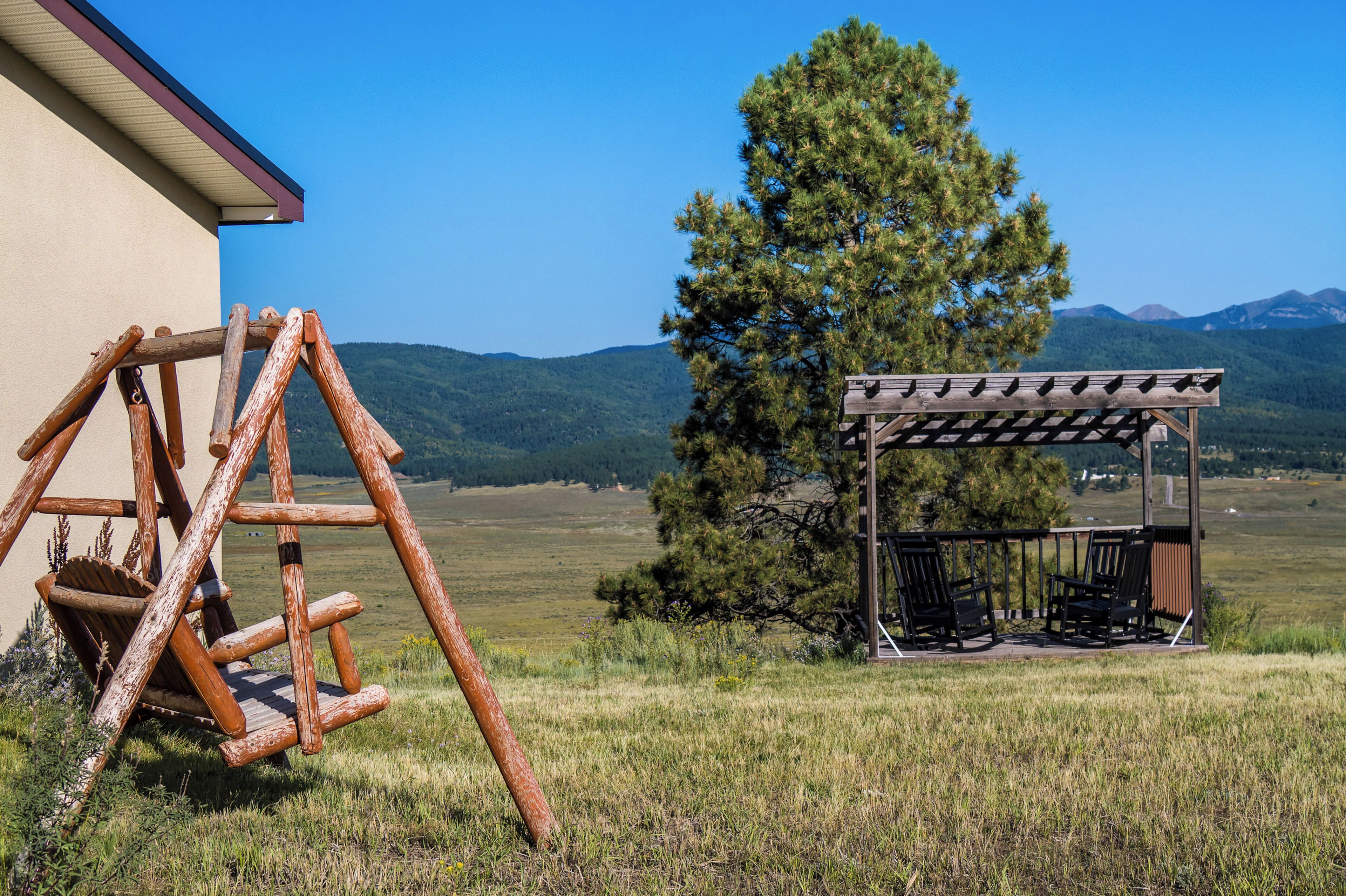 Un ensemble de balançoires en bois et un espace de repos couvert offrant une vue sur une chaîne de montagnes.