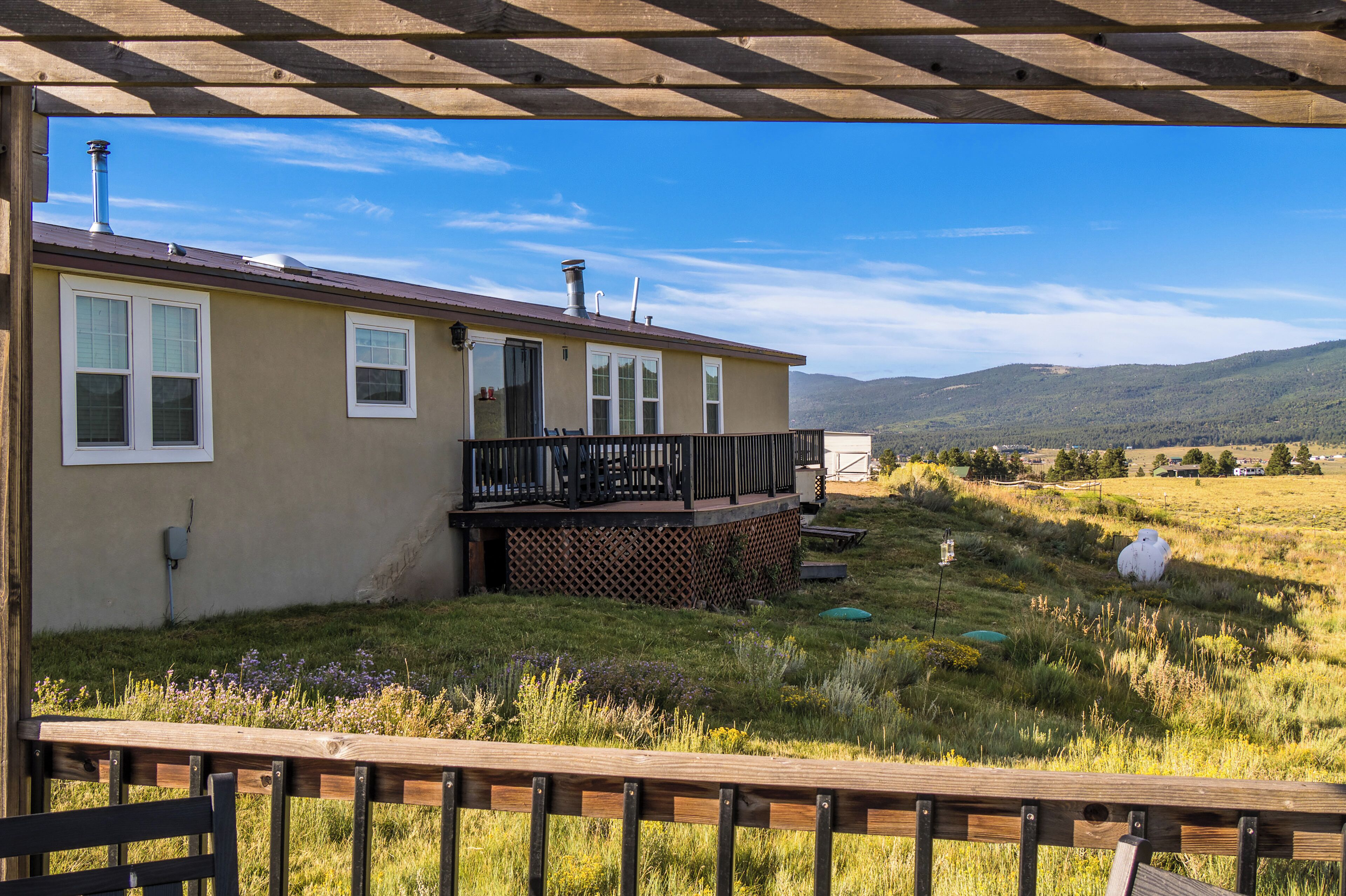 A house with a deck, a chimney, and a view of a grassy field and hills.