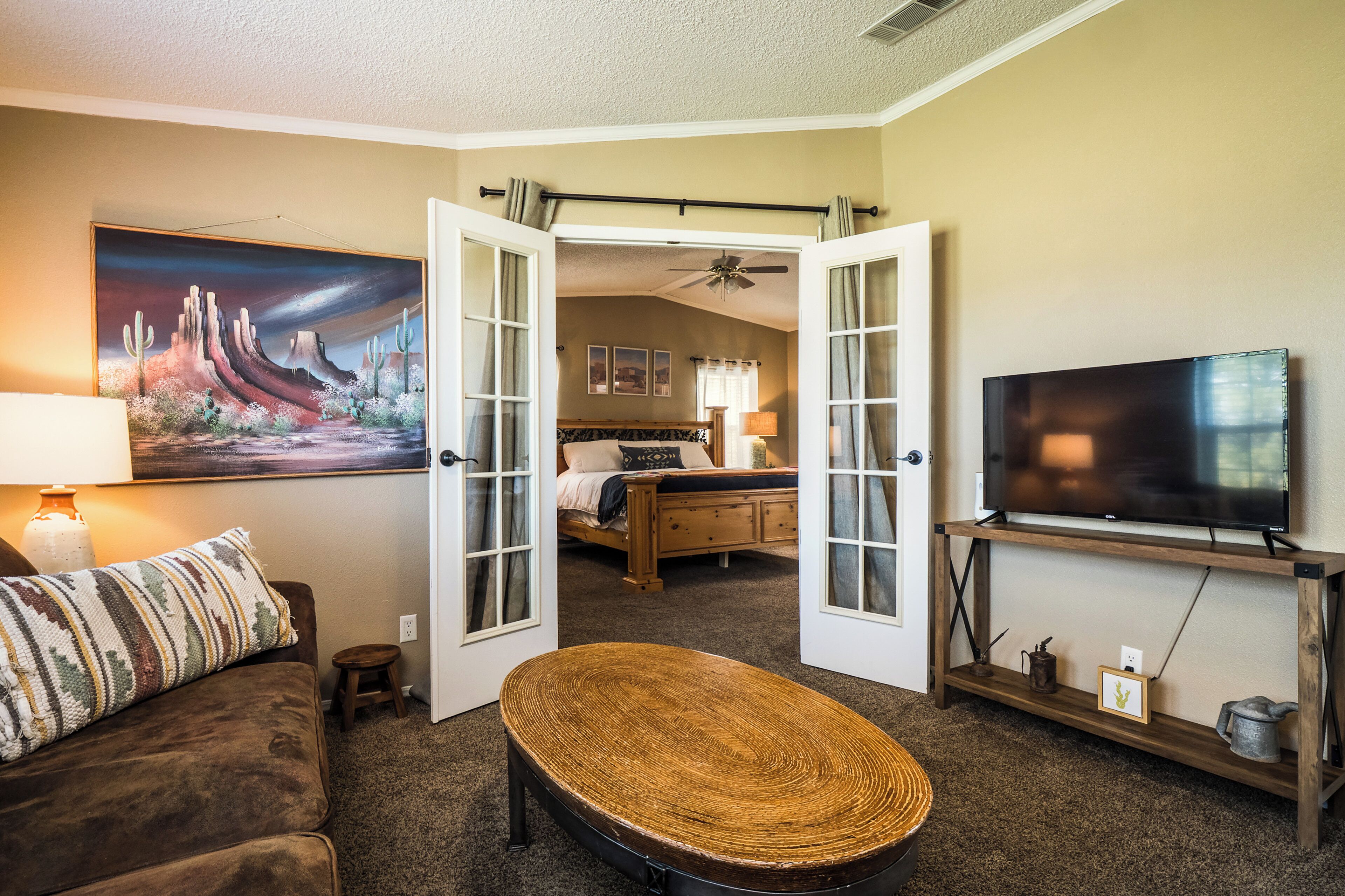 A cozy living room with a sofa, a woven coffee table, a television on a wooden stand, and a painting on the wall.