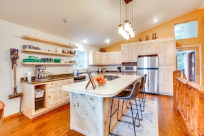 A modern kitchen with wooden cabinets, a central island, bar stools, and a hanging light fixture. - Cozy Angel Fire Vacation Rental: 4 Mi to Resort! (Angel Fire)