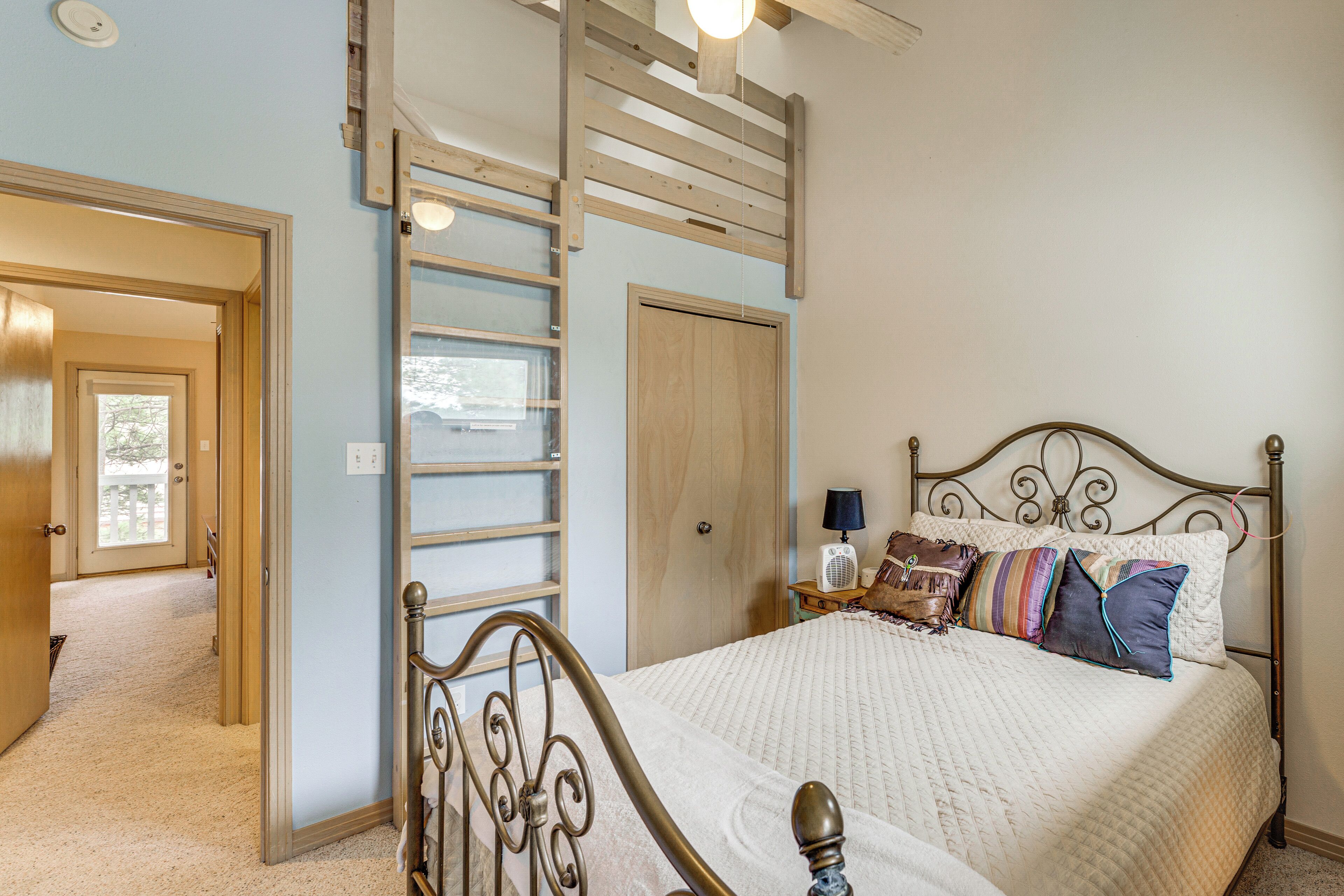 A bedroom with a bed, a wooden ladder, a nightstand, and a door leading to another room.