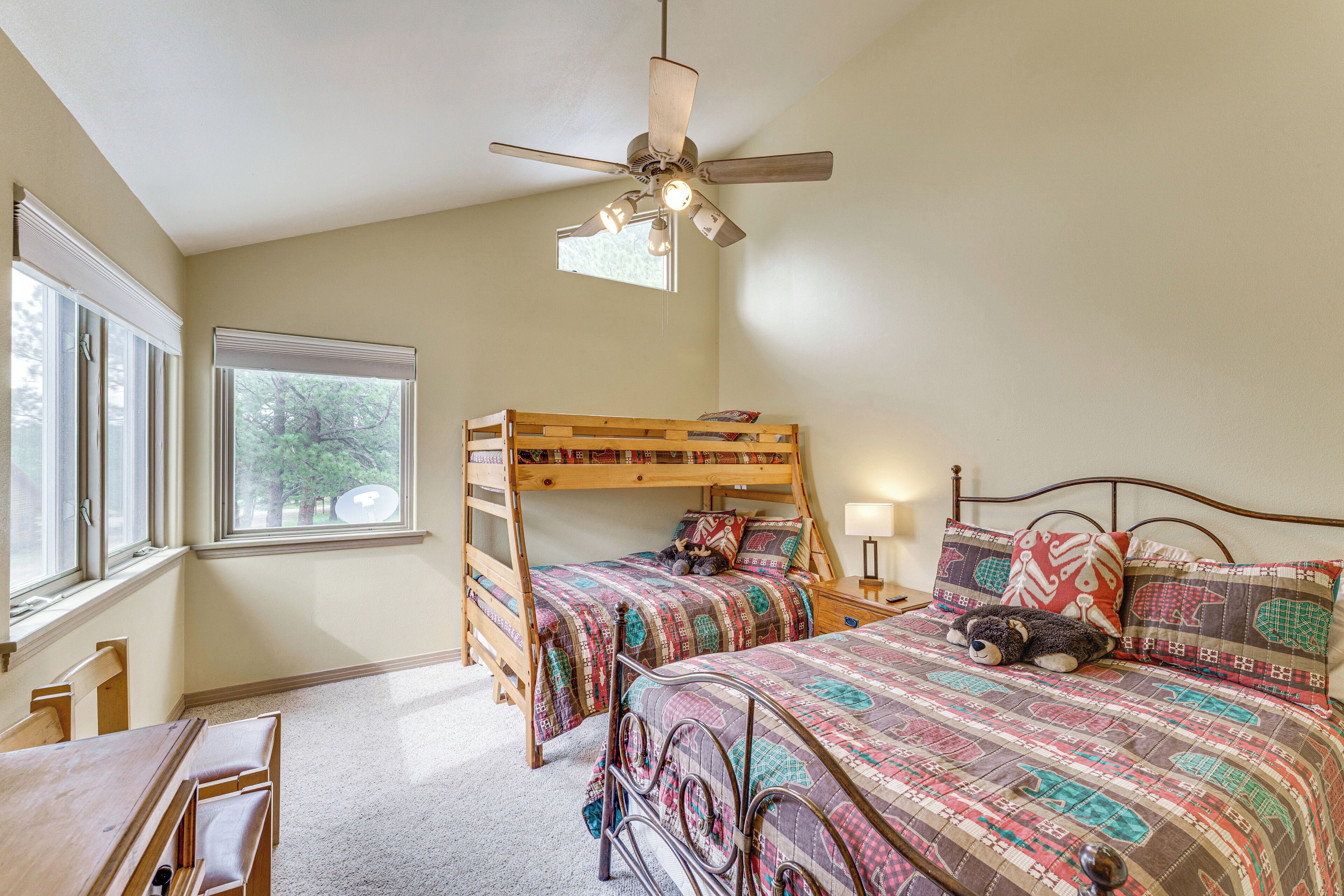 A bedroom with bunk beds, a desk, and a window with a view of trees.