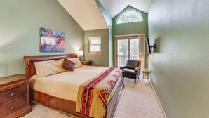 A bedroom with a large bed, a wooden nightstand, a chair, and a window with a view of trees. - Half Mi to Angel Fire Resort: Townhome w/ Grill! (Angel Fire)