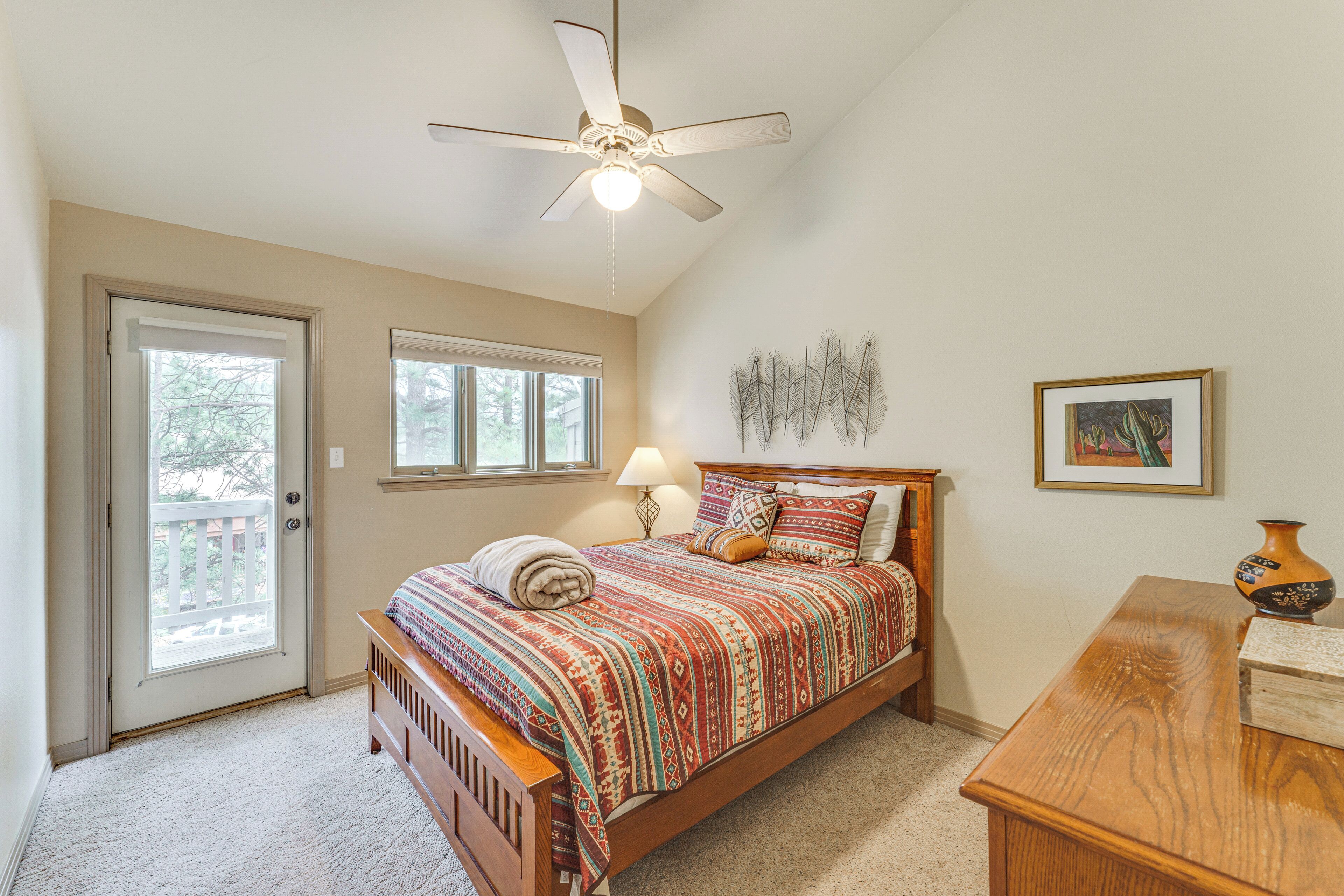 A bedroom with a bed, a ceiling fan, a door leading to a balcony, and a small table with a vase.