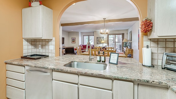A kitchen with a granite countertop, a sink, and a built-in dishwasher. There is a dining area visible through an archway. - Half Mi to Angel Fire Resort: Townhome w/ Grill! (Angel Fire)