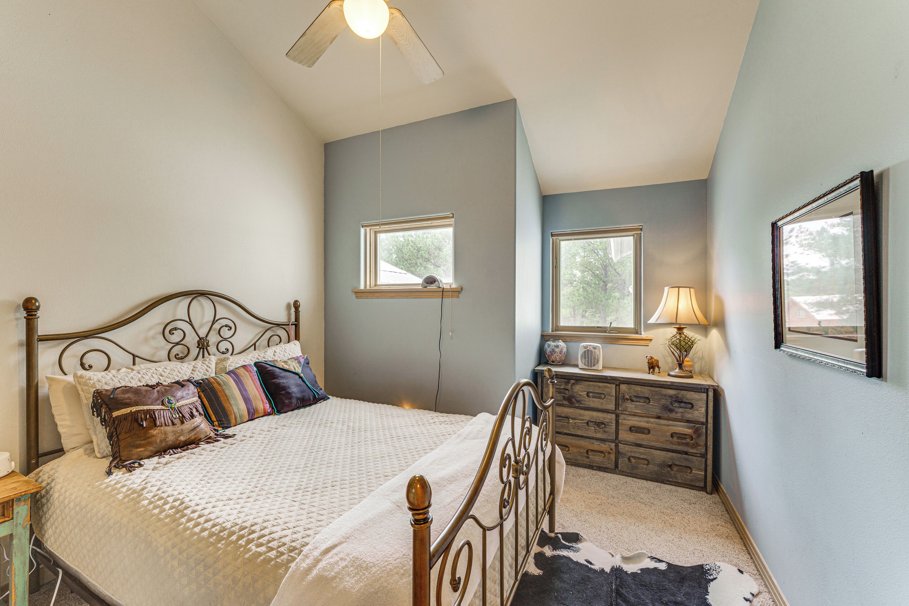 A bedroom with a bed, dresser, two windows, and a ceiling fan.