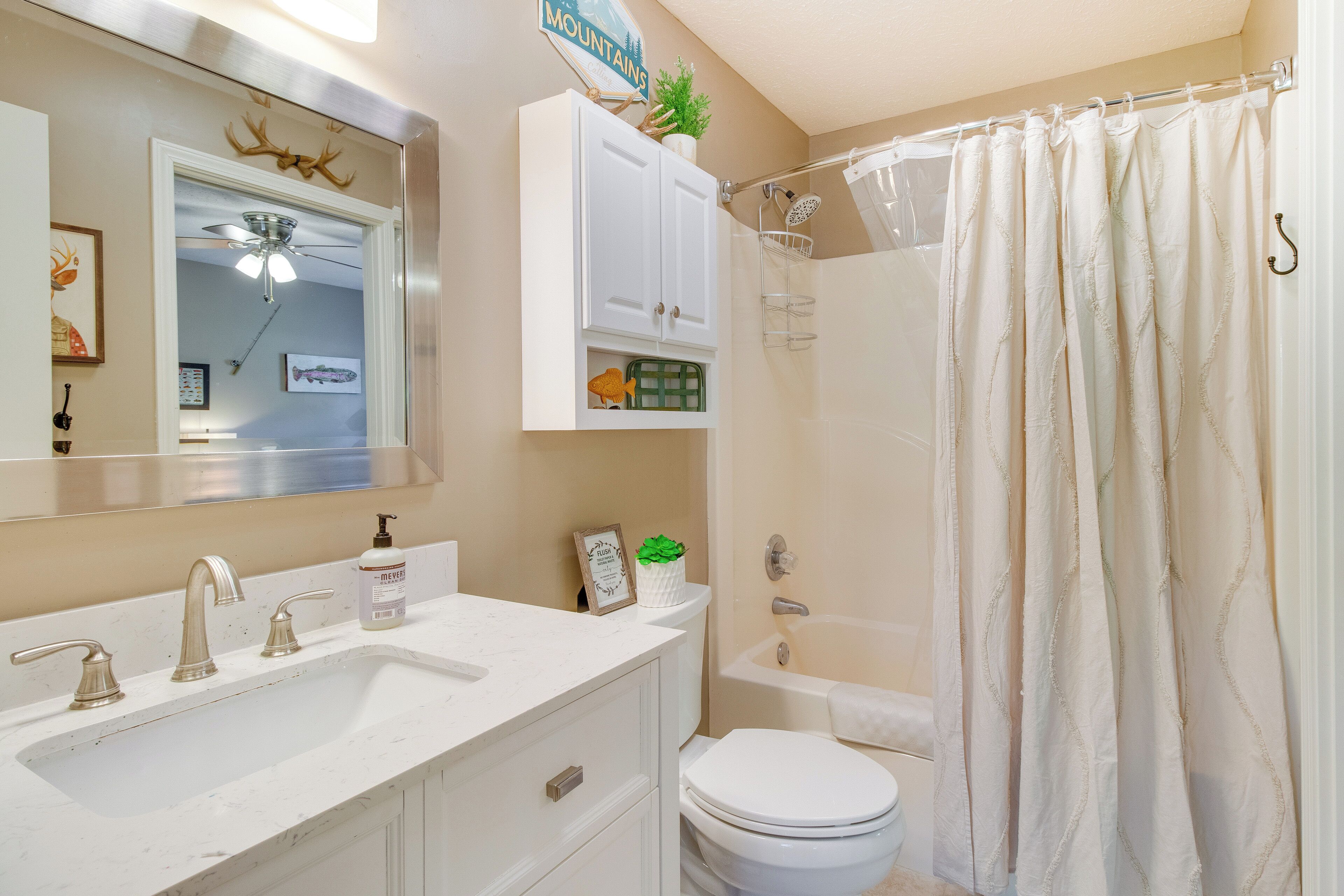 Un baño con lavamanos, tocador, inodoro y cortina de ducha blanca.