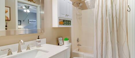 Un baño con lavamanos, tocador, inodoro y cortina de ducha blanca.