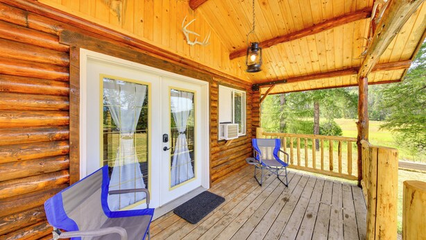 A wooden cabin with a porch, two sliding glass doors, a wooden deck, and a deer antler decoration. - Cozy Farm Cabin - 9 Mi to Trout Creek! (Trout Creek)