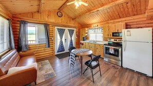 A cozy cabin interior with a sofa, dining table, chairs, a kitchen area with appliances, and a ceiling fan. - Cozy Farm Cabin - 9 Mi to Trout Creek! (Trout Creek)