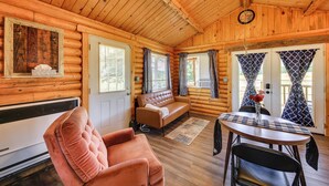 A log cabin interior with a sofa, a table with chairs, a ceiling fan, and a clock on the wall. - Cozy Farm Cabin - 9 Mi to Trout Creek! (Trout Creek)