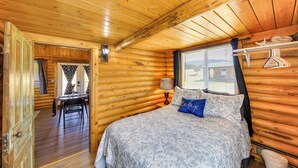 A wooden cabin interior with a bed, a desk, and a window with curtains. - Cozy Farm Cabin - 9 Mi to Trout Creek! (Trout Creek)