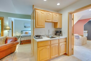 A compact kitchen with wooden cabinets, a sink, and a stove. There is a small island with a sink and a coffee maker. The room has a bed with a headboard and a lamp. - Charming Stockholm Abode in Walkable Location! (Stockholm)