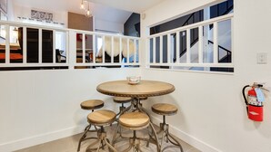 A dining area with a round table and four stools, a fire extinguisher on the wall, and a staircase with a view of the upper floor. - Chic Angel Fire Condo: Walk to Ski Resort! (Angel Fire)