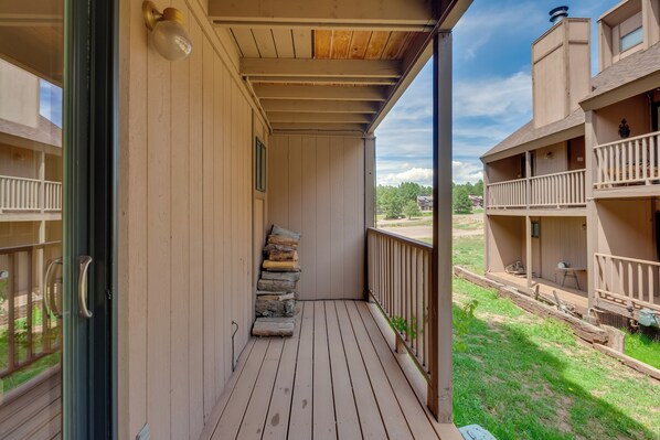 A wooden balcony with a stack of firewood, a glass door, and a view of a green landscape. - Chic Angel Fire Condo: Walk to Ski Resort! (Angel Fire)