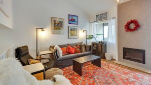 A living room with a sofa, armchair, and coffee table, a fireplace, and wall-mounted artwork. - Chic Angel Fire Condo: Walk to Ski Resort! (Angel Fire)