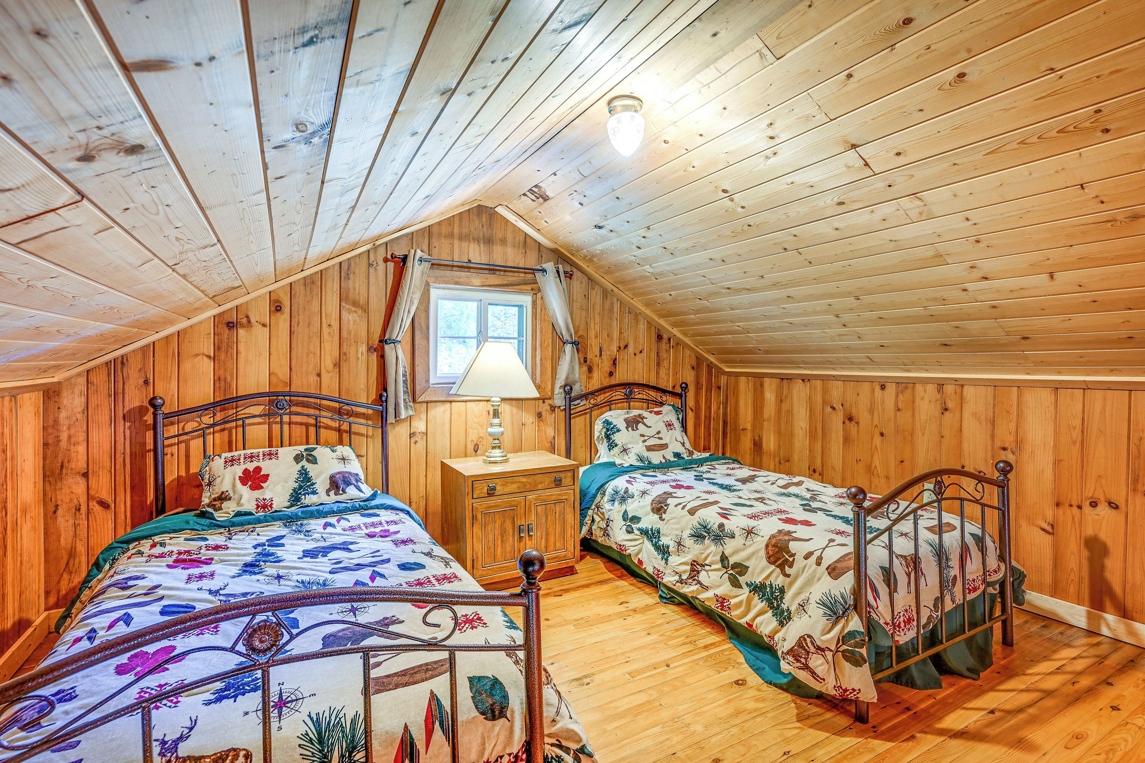 A cozy attic bedroom with two wooden beds, a nightstand, and a window.