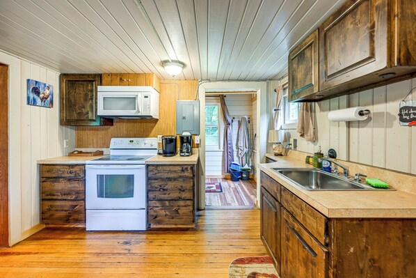 A kitchen with wooden cabinets, a white stove, a microwave, and a sink.