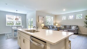A modern kitchen with a central island, a dining area with a table and chairs, and a living area with a sofa and lamps. - 3 Mi to Bethany Beach: Ocean View Home w/ Patio (Ocean View)