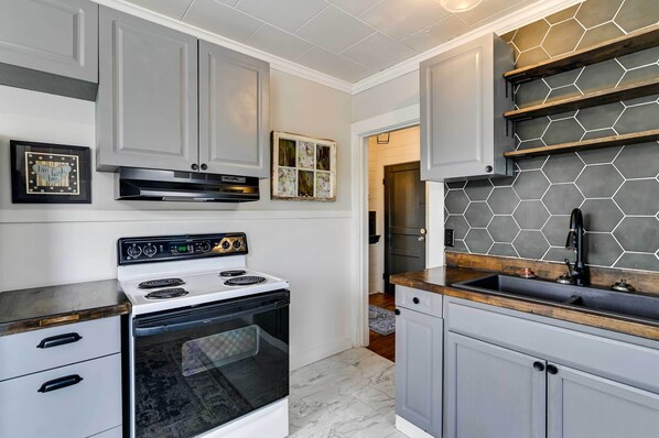 A kitchen with a white stove, grey cabinets, and a hexagonal tile backsplash.