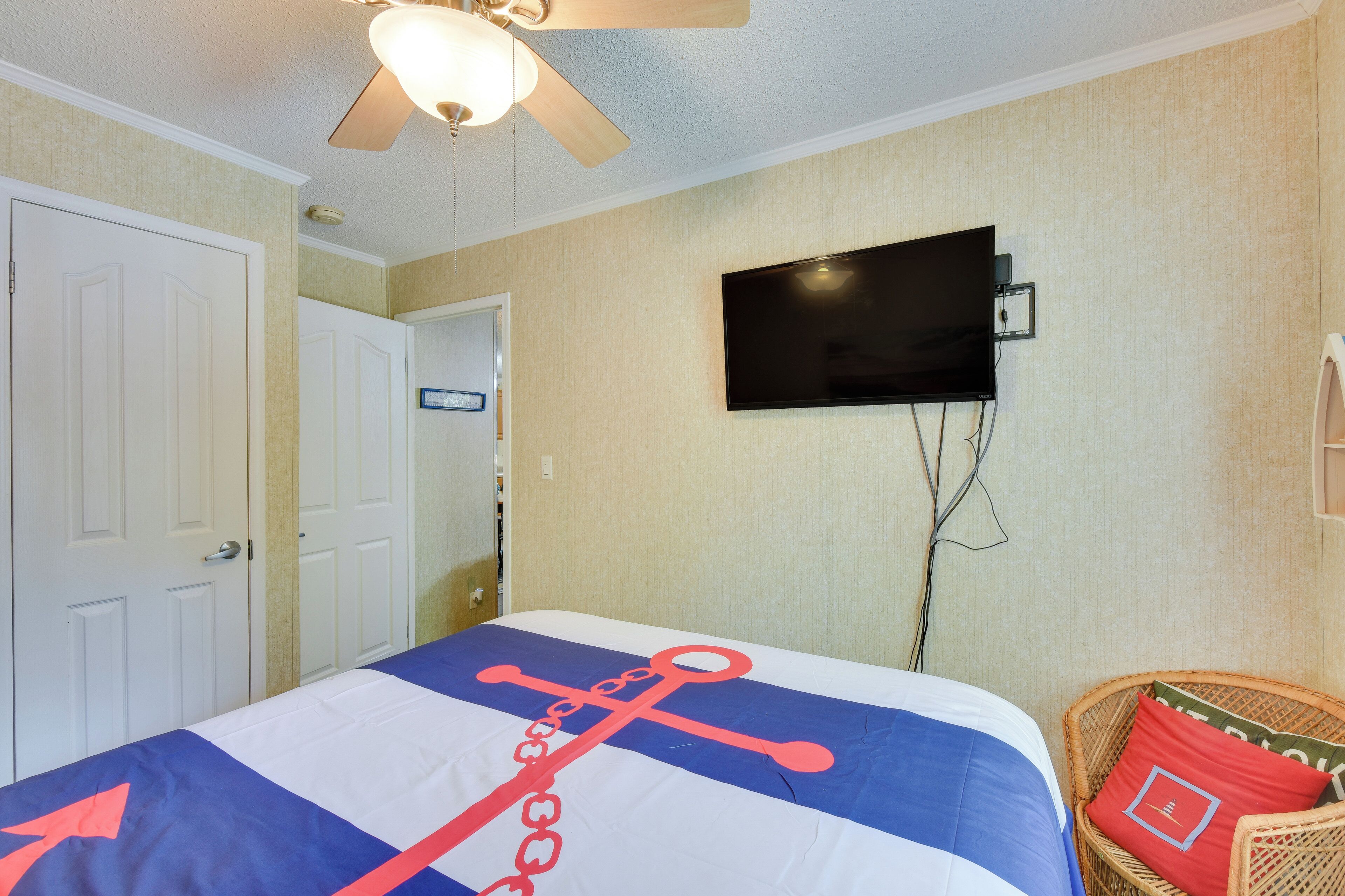 A hotel room with a bed, a television mounted on the wall, a ceiling fan, and a door.