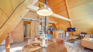 Un loft spacieux avec de hauts plafonds, des murs en bois, une table ronde centrale, un canapé, un téléviseur et un coin cuisine.