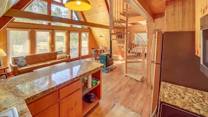 Une cuisine spacieuse dotée d’un grand îlot central, de meubles en bois et d’une cuisinière intégrée. On y trouve également un coin salon confortable avec un canapé et une table à manger.