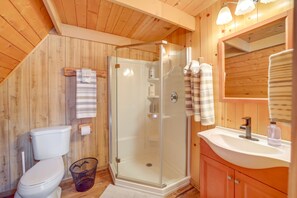 A wooden-paneled bathroom with a glass-enclosed shower, a white toilet, and a sink with a mirror. - Pet-friendly Arizona Cabin - Fire Pit, Near Skiing (Munds Park)