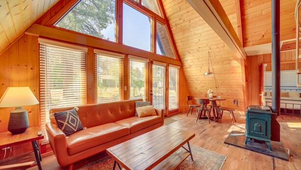 Une pièce confortable de style loft, avec un plafond en bois, de grandes fenêtres, un canapé en cuir, une table en bois et un poêle à bois.