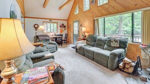 Un intérieur de chalet chaleureux avec une cheminée, des poutres en bois au plafond et de grandes fenêtres.