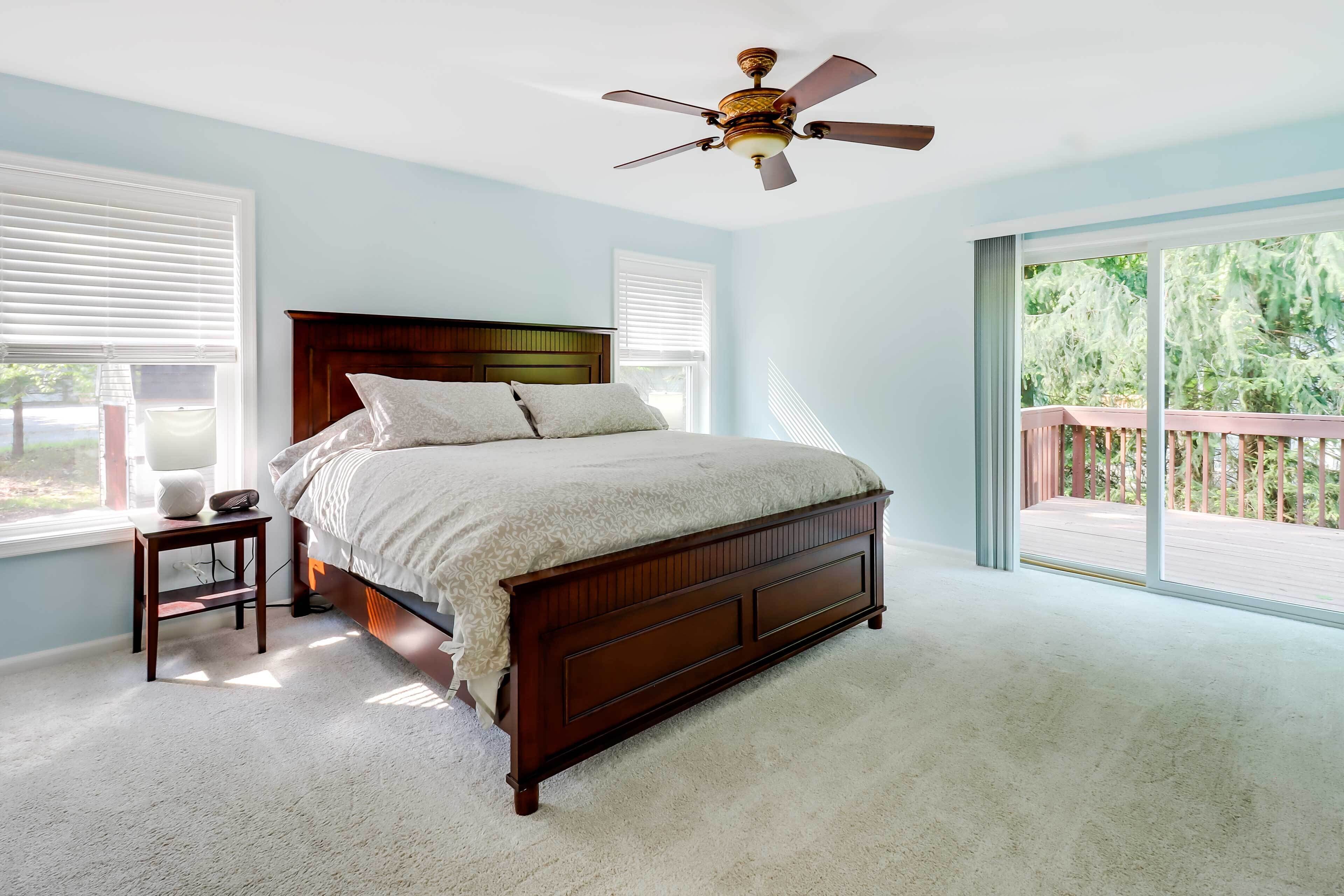 Quarto com uma cama grande, mesa de cabeceira, ventoinha no teto e vista para um deck através de uma porta de correr de vidro.