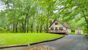 Une cabane dotée d’une terrasse et d’un petit abri, entourée d’arbres verdoyants et d’une zone herbeuse.