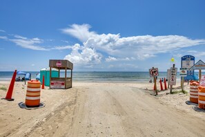 A beach with a sandy path, beach huts, and signs indicating beach rules and no class allowed.