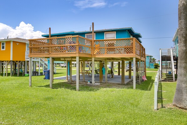 A two-story wooden structure with a balcony, surrounded by grass and other buildings.