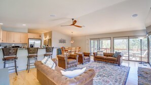 A spacious living area with a large brown leather sofa, a dining table with chairs, and a kitchen area with wooden cabinets and a refrigerator.