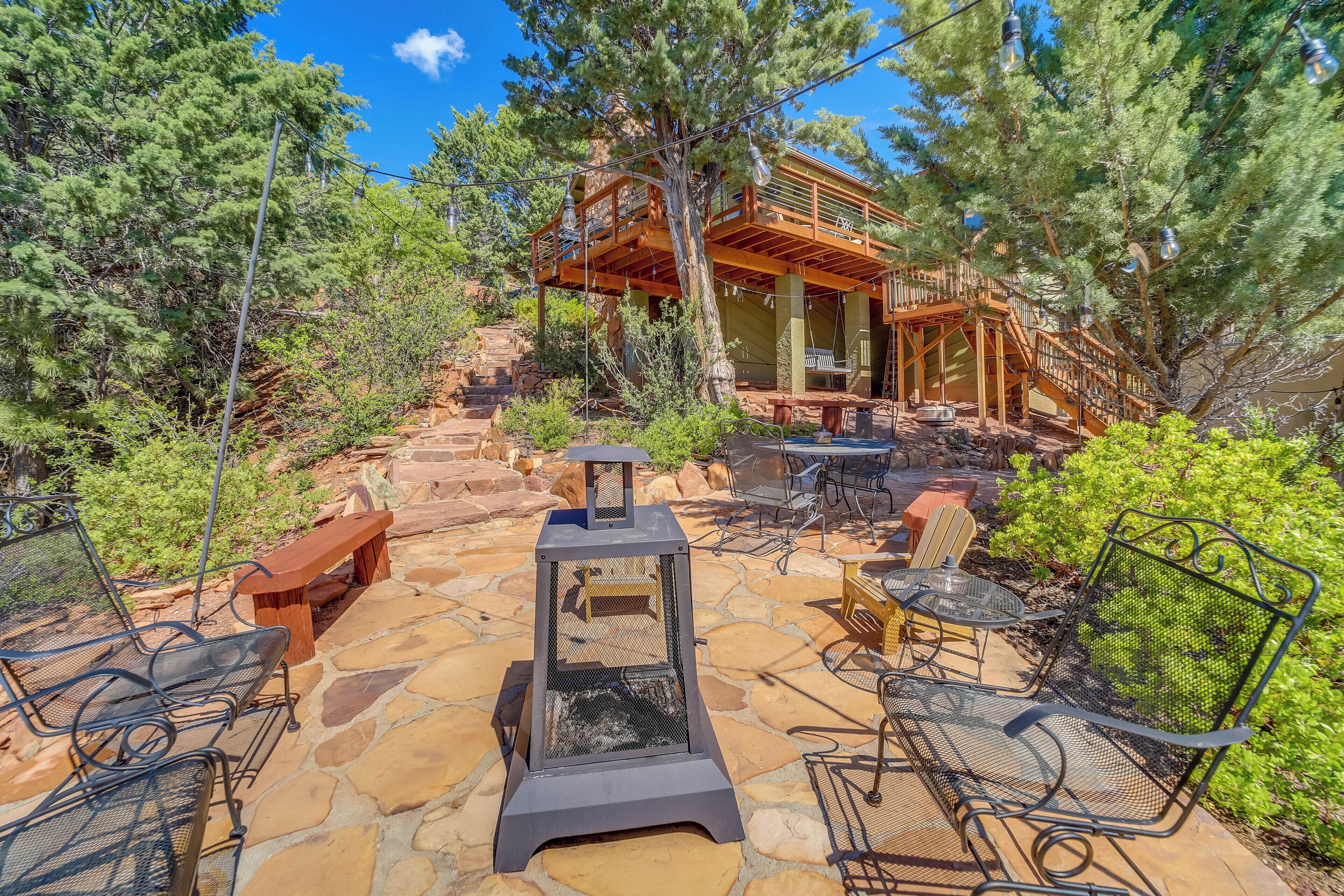 A patio area with stone flooring, outdoor furniture, and a wooden deck with a staircase leading to a house.