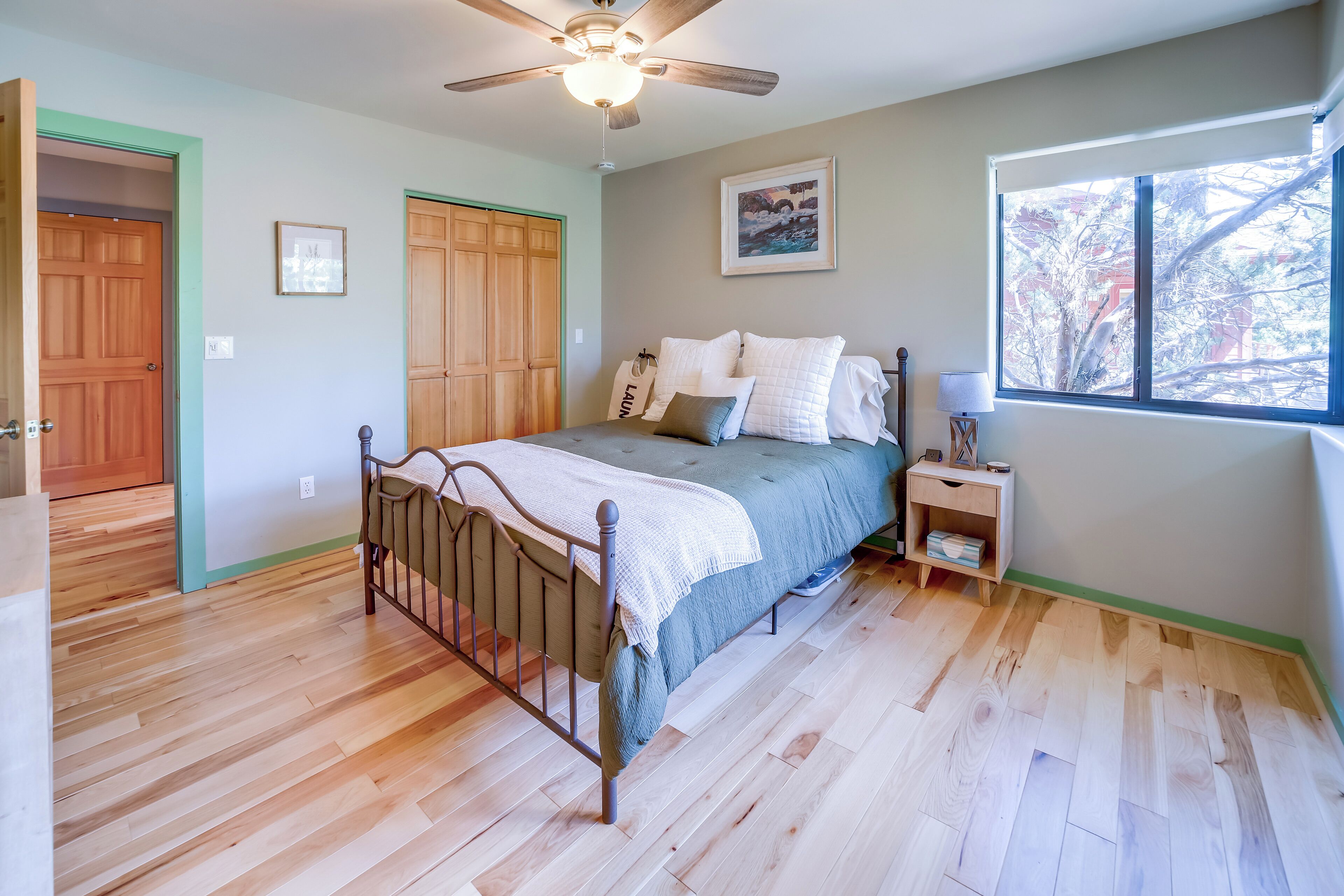 A bedroom with a bed, a nightstand, a ceiling fan, a window, and wooden flooring.