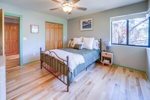A bedroom with a bed, a nightstand, a ceiling fan, a window, and wooden flooring.