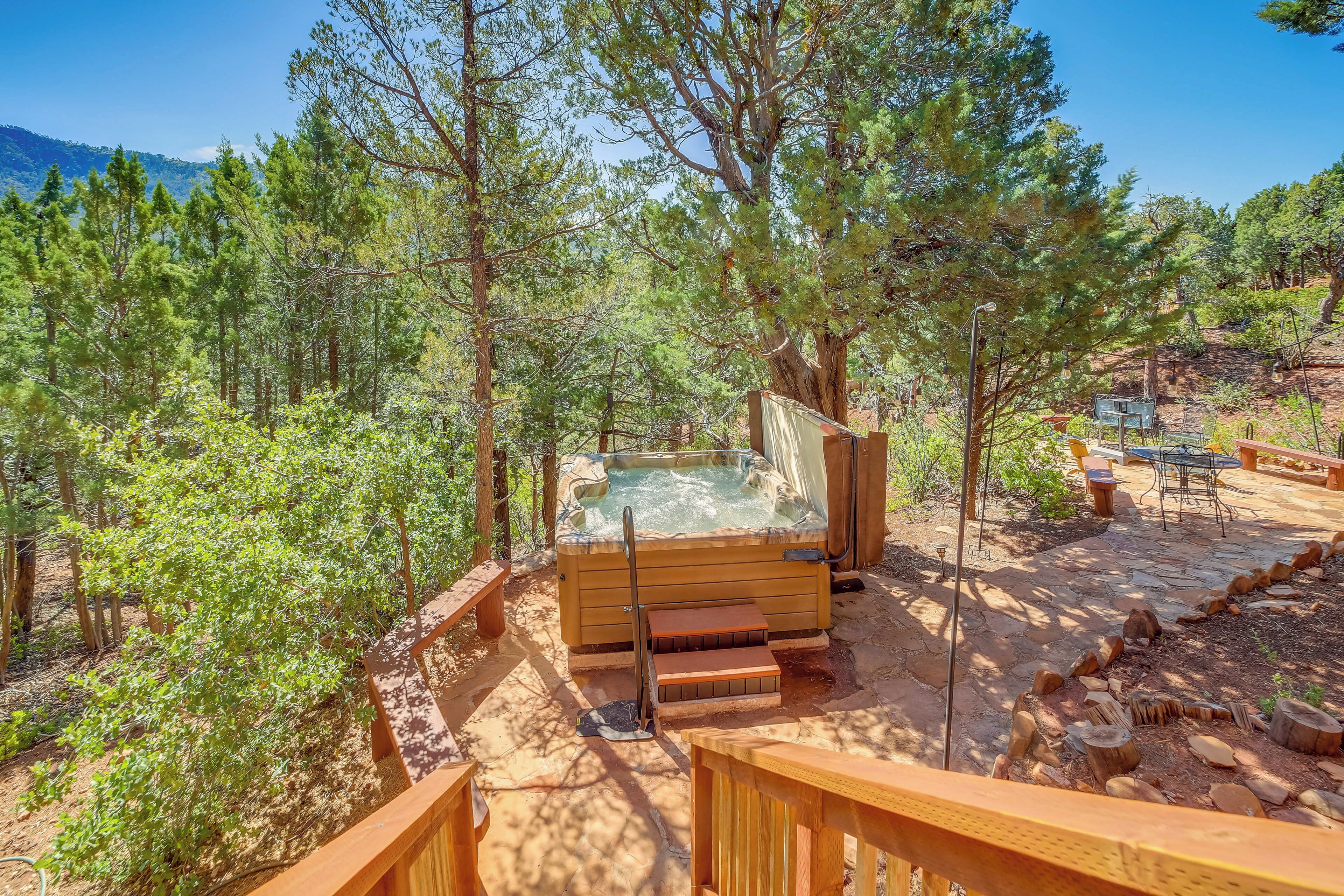 Ein Whirlpool, umgeben von einer Holzterrasse und Steinstufen, eingebettet in eine bewaldete Landschaft mit Kiefern.