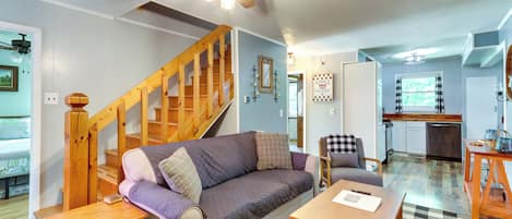 A cozy living room with a wooden staircase, a checkered floor, a sofa, and a dining table.