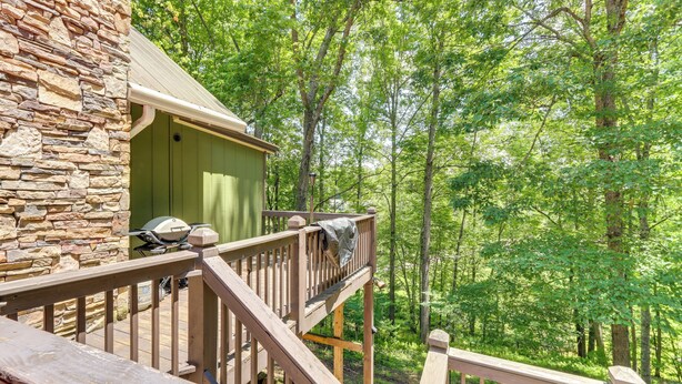 A wooden deck with a stone wall, a covered outdoor area, and a forested backdrop. - Pet-friendly Murphy Home: Grilling Deck + Fire Pit (Murphy)