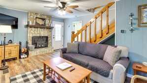 A living room with a stone fireplace, a wooden staircase, a sofa, and a ceiling fan. - Pet-friendly Murphy Home: Grilling Deck + Fire Pit (Murphy)