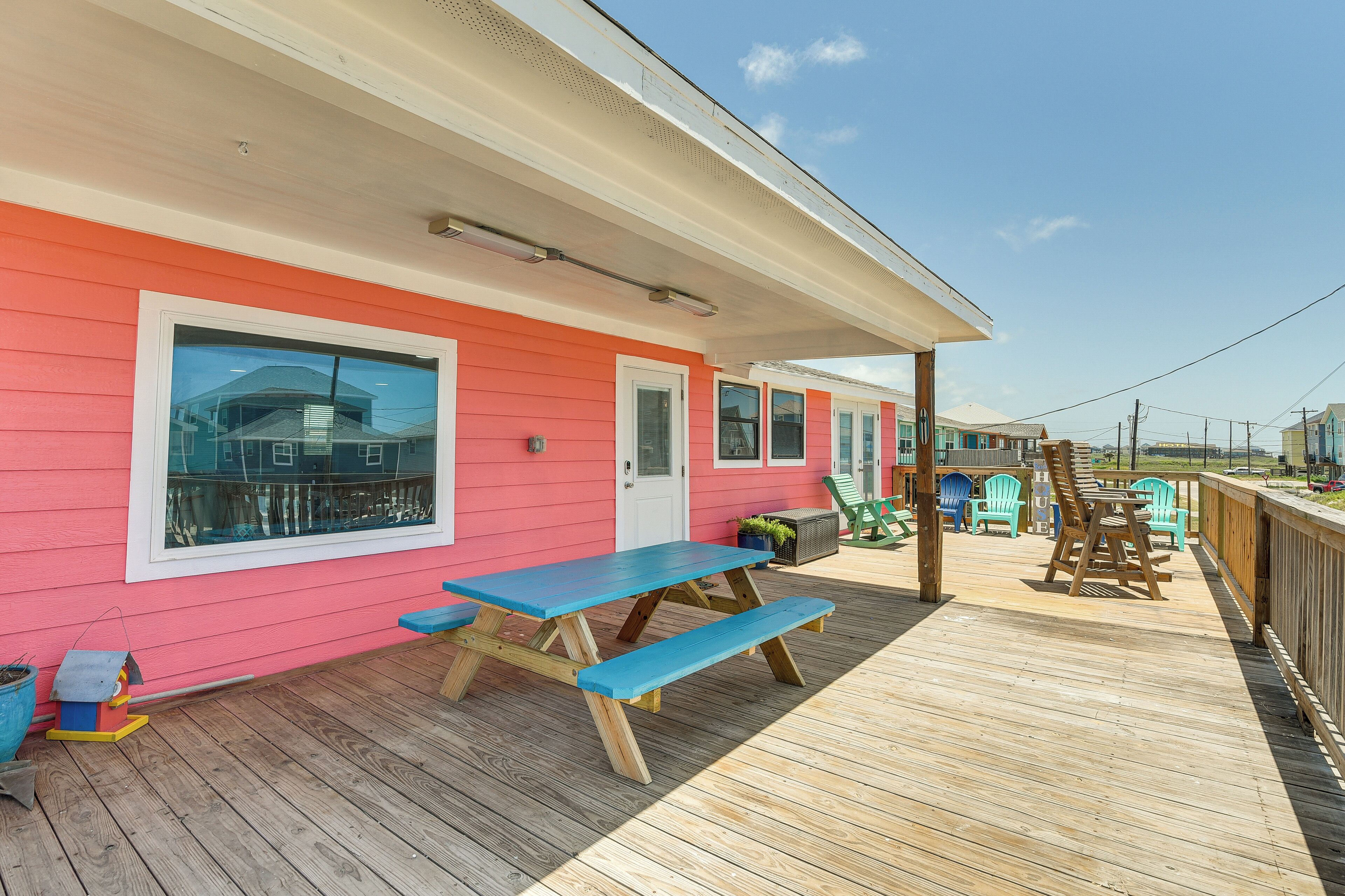 A wooden deck with a picnic table and benches, a covered area with chairs, and a view of the ocean.