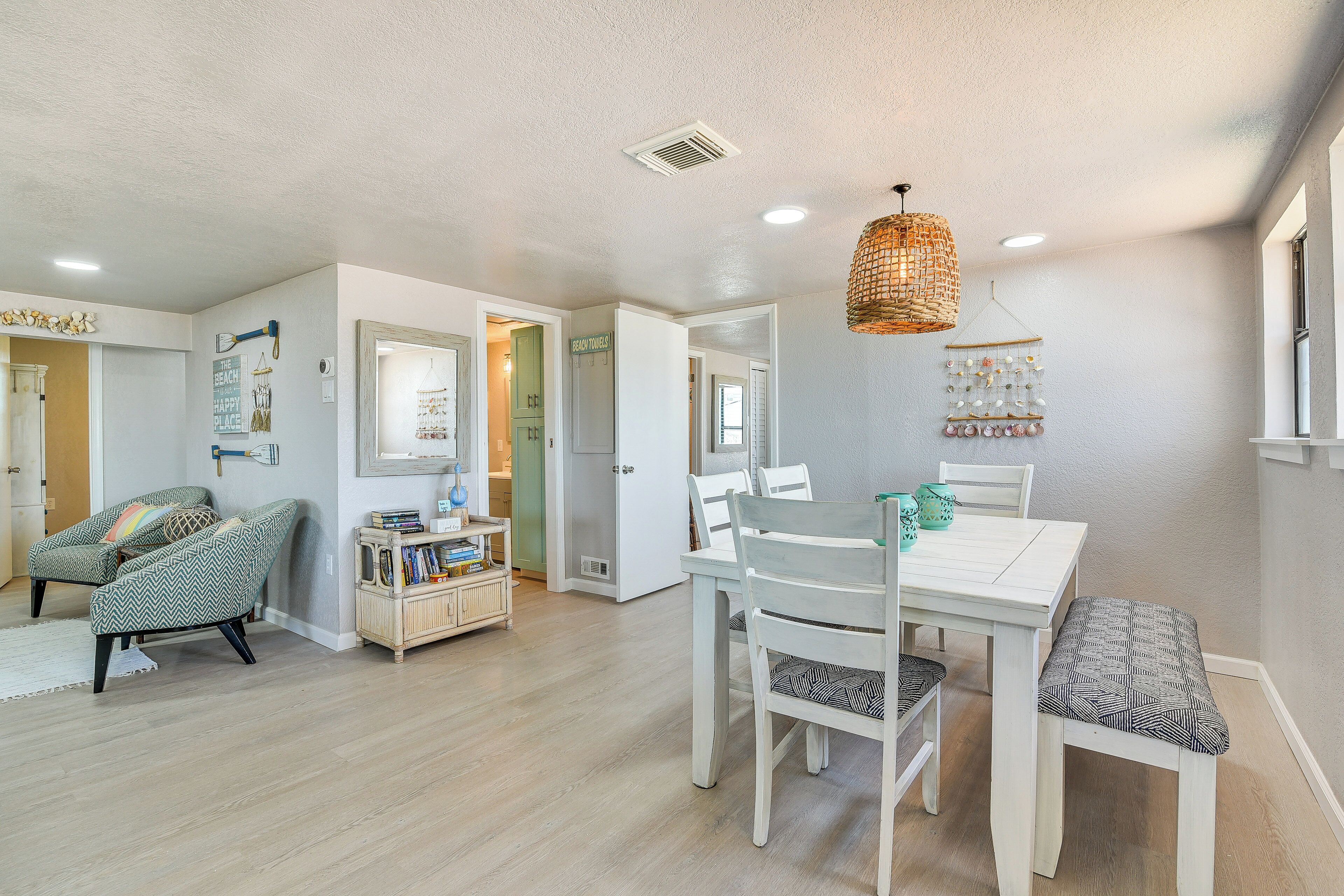 A spacious living area with a dining table, chairs, and a bench. There is a bookshelf and a decorative wall hanging.