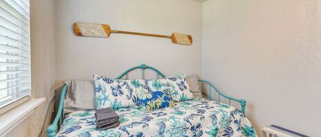 A bedroom with a bed, a window with blinds, and a wall-mounted wooden object.