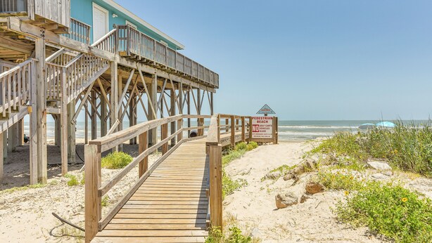 Una passerella di legno che conduce a una casa sulla spiaggia con un balcone vista oceano.